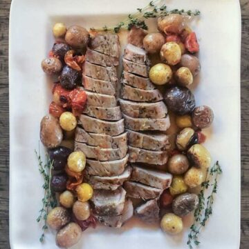 Pork tenderloin on a platter with baby potatoes and tomatoes.
