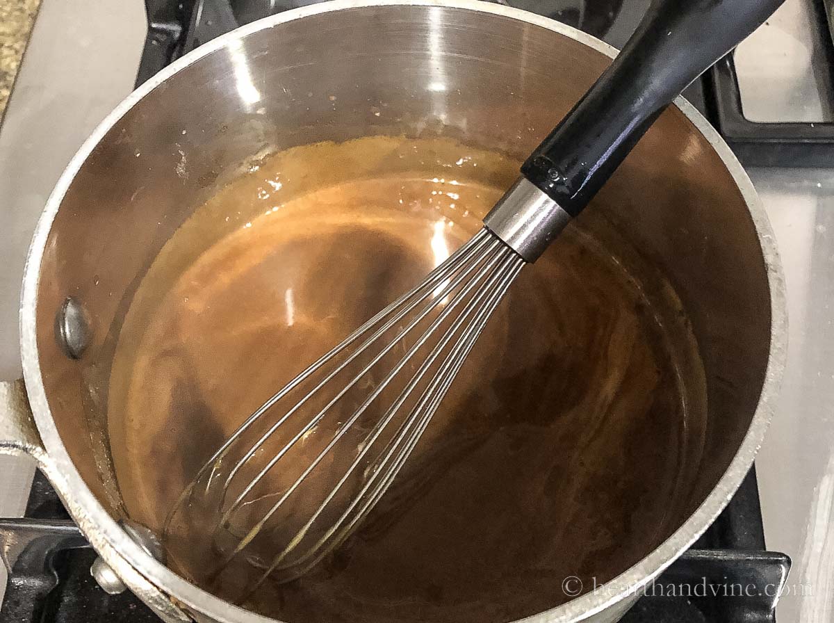 Brown gravy in a sauce pan on the stove with a whisk.