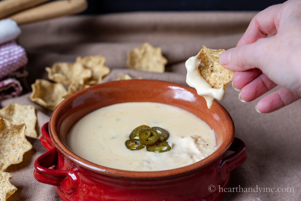 Queso dip in a red bowl with sliced jalapenos and a scoop tortilla lifting some of the sauce.