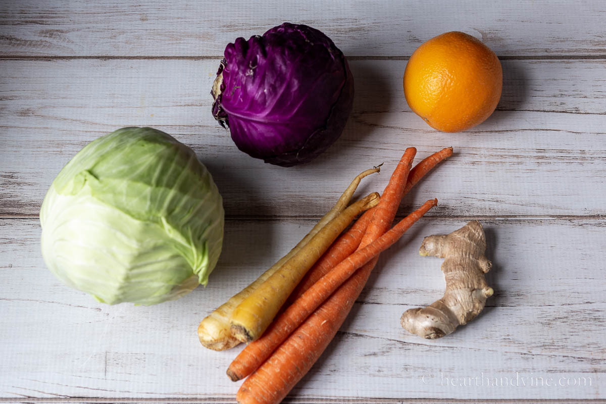 Head of green cabbage, head of red cabbage, several carrots, an orange and some ginger root.