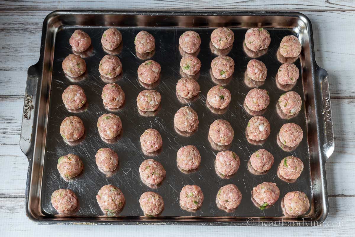 Raw meatballs on a grease baking sheet.