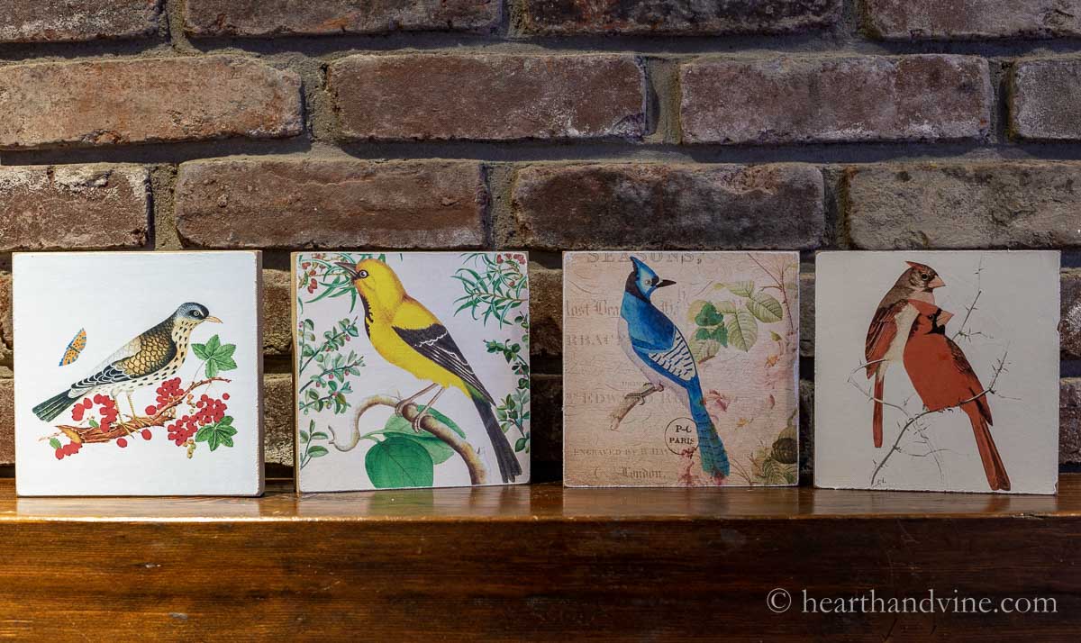Four large bird images on wood blocks on a mantel.