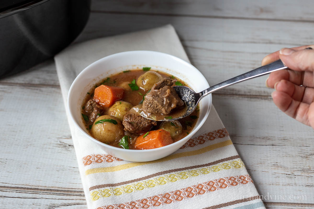 A small bowl filled with Irish stew with a large spoon lifting a bite.