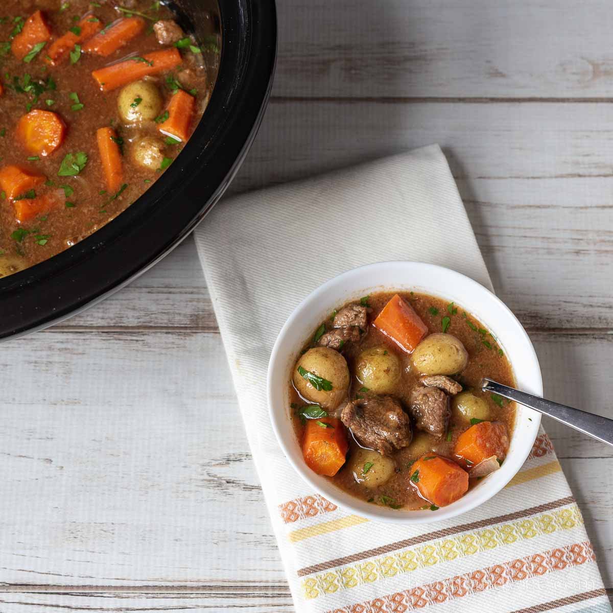 Small white bowl filled with Irish beef stew next to a crockpot of the same.