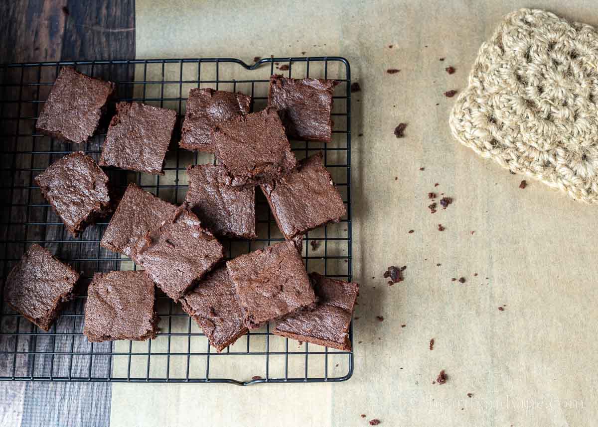 Brownies on a cooling rack with bits of brown scattered and a pot holder.