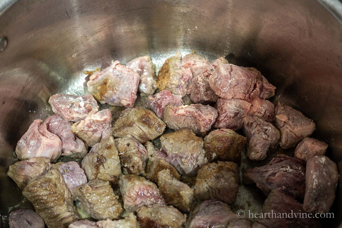 Browning beef cubes in a large pot on the stove.