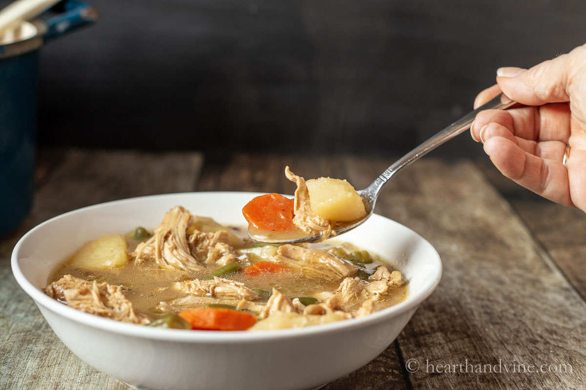 Bowl of chicken stew with a spoon taking a bite.