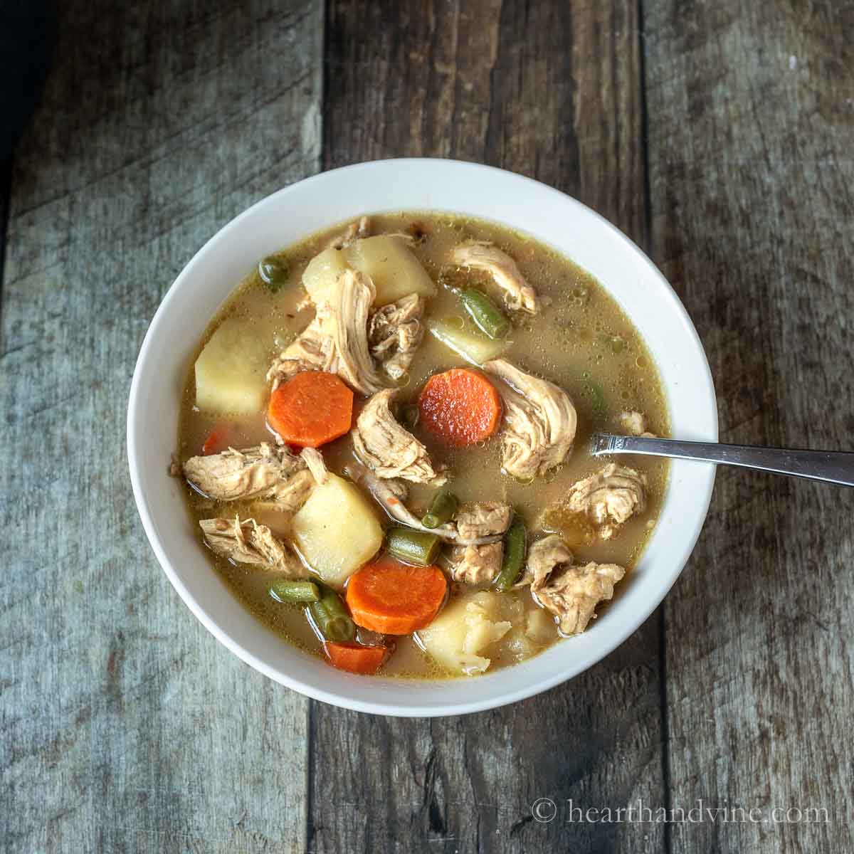 White bowl of chicken stew with a spoon.