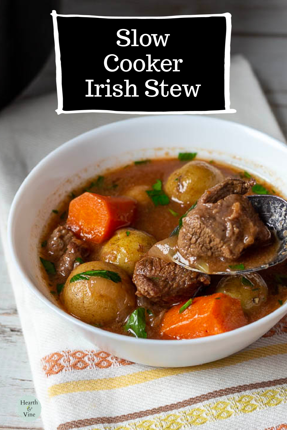 A spoon taking a bite of Irish beef stew in a white bowl.