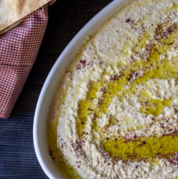 Hummus dip in a serving platter next to a basket of pita wedges.