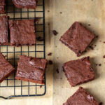 Brownies on a cooling rack and a few next to it on parchment paper.