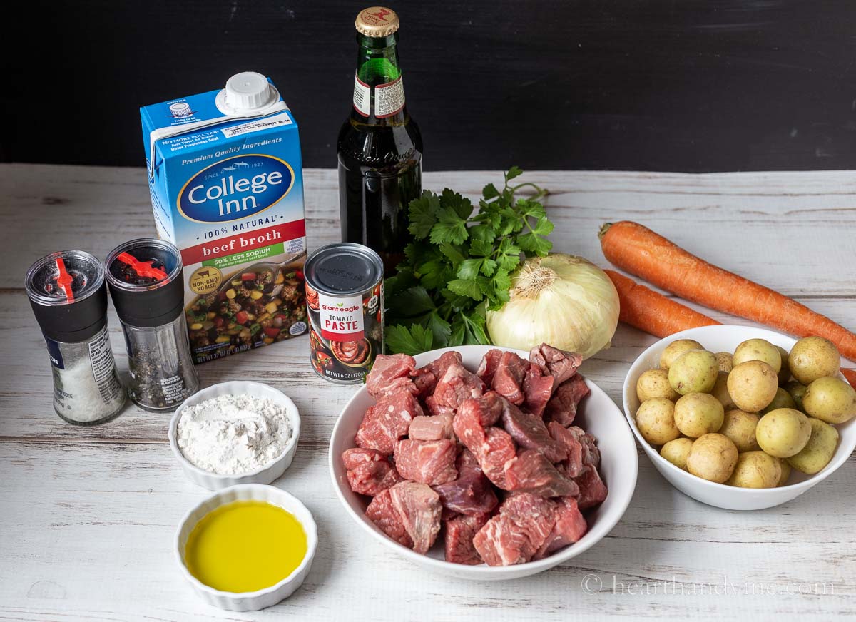 Ingredients for Irish beef stew including beef cubes, potatoes, carrots, onions, beer, broth, flour, oil, parsley, tomato paste, salt and black pepper.