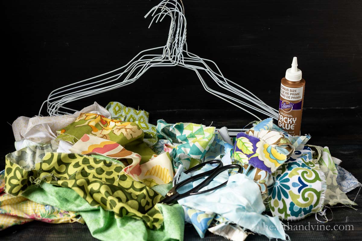 Supplies for fabric wrapped hangers including glue, white wired hangers, scissors and leftover fabric scraps.