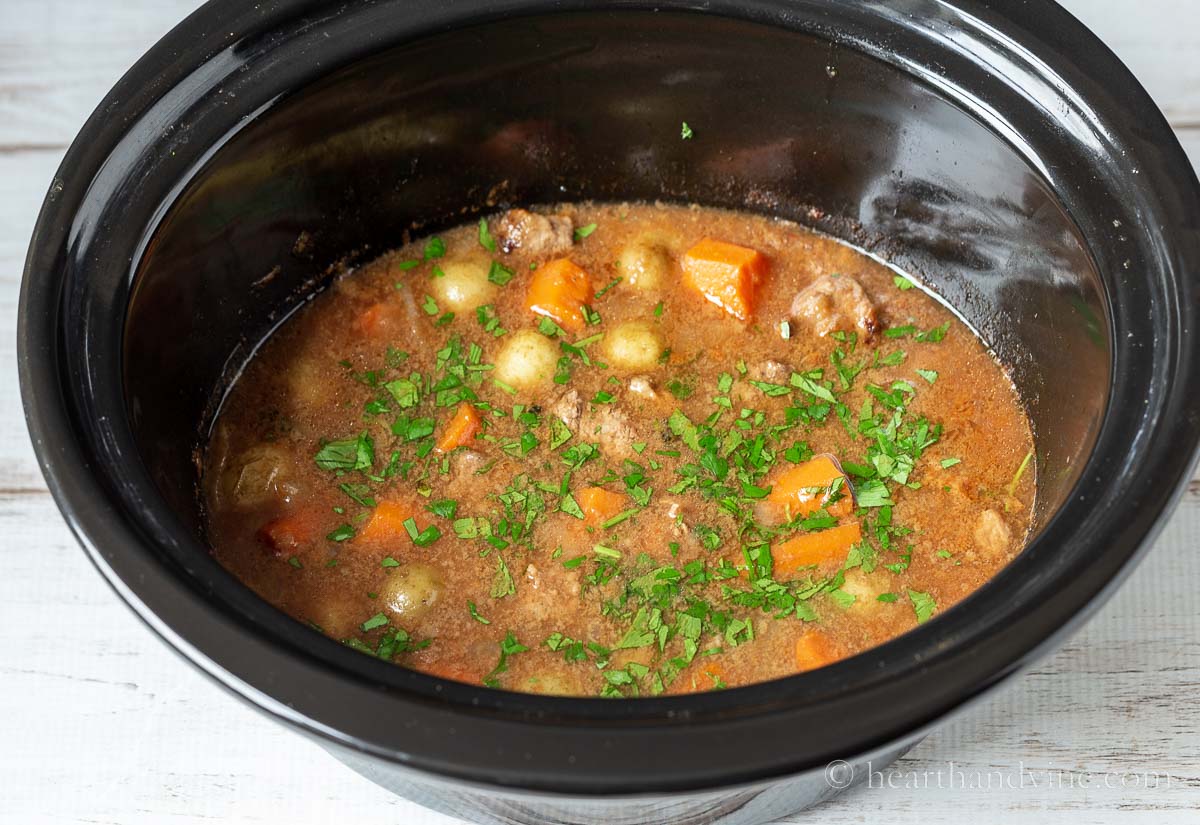 Slow cooker pot with Irish beef stew after cooking with fresh parsley sprinkled over top.