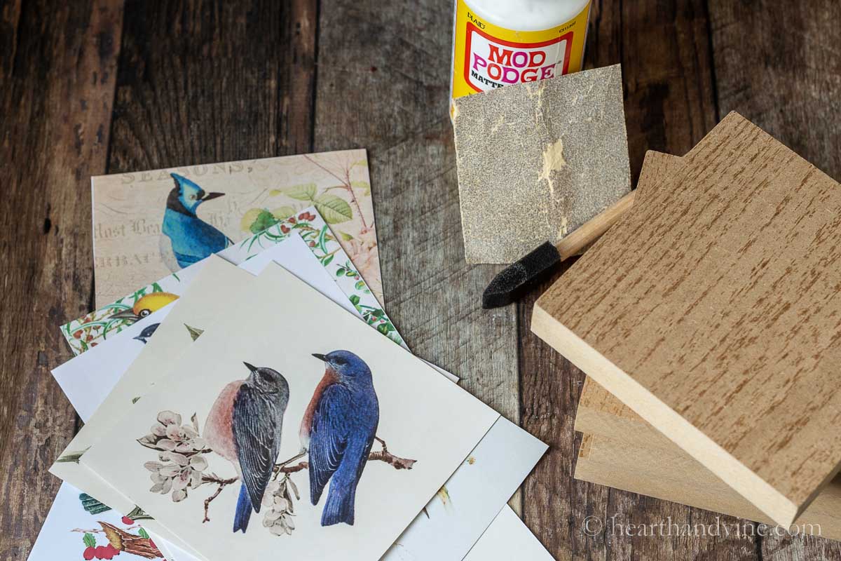 Supplies for DIY wood block art including mod podge, bird prints, wood blocks, sponge brush and sandpaper.