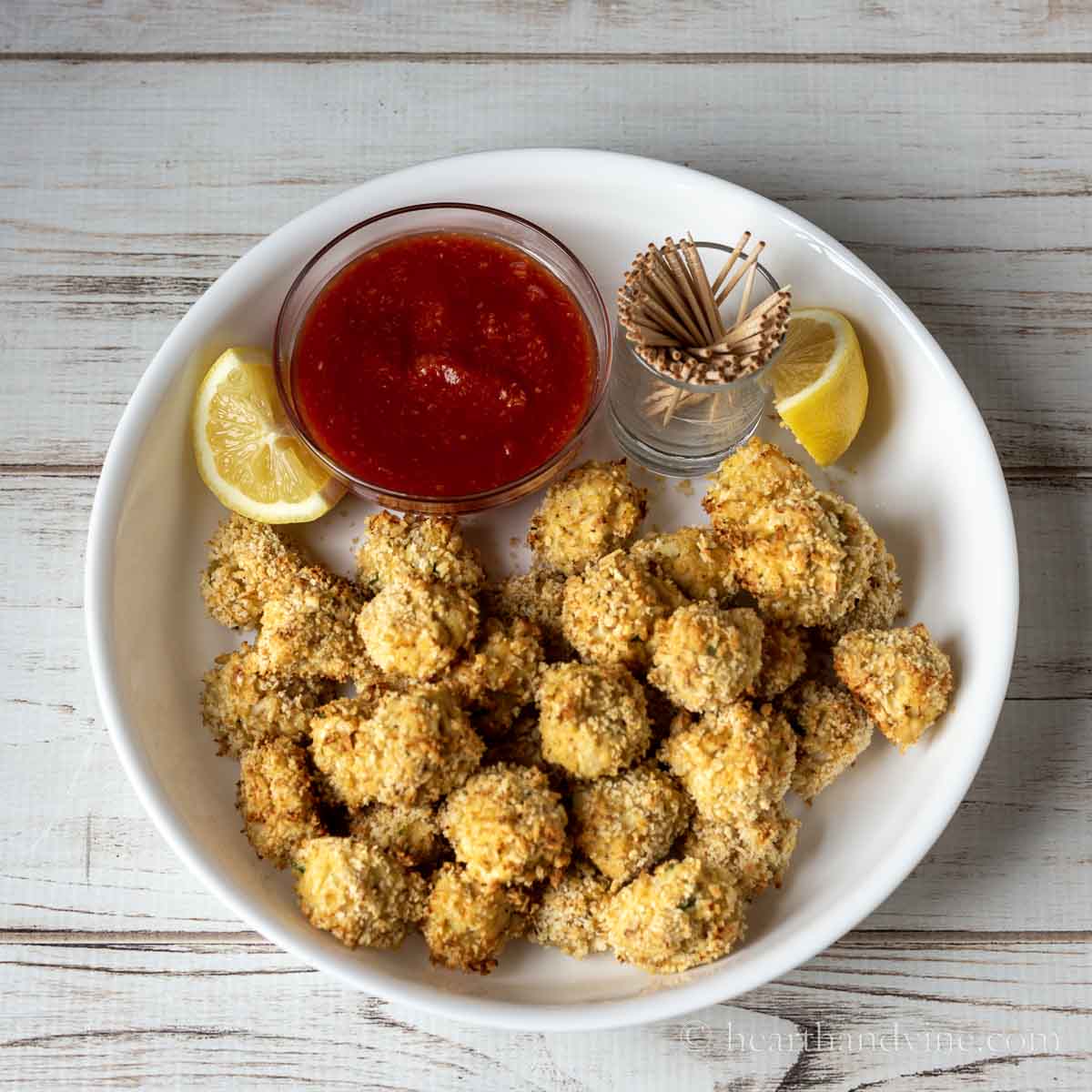 Bowl of crab balls with lemon wedges and cocktail sauce on the side.