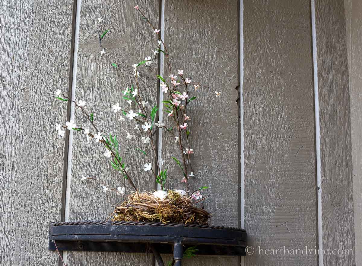 A handmade nest with two fake speckled eggs on a shelf. Faux spring blossoms standing behind.