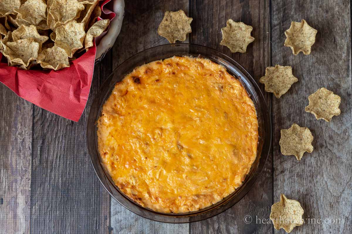 Baked buffalo chicken dip with a basket of chips and a few scattered chips.