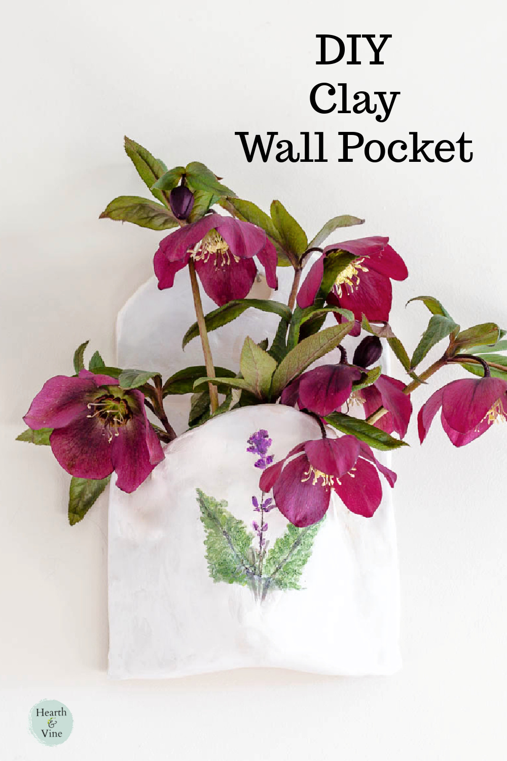 Close up of diy clay wall pocket hanging with dark purple hellebore flowers inside.