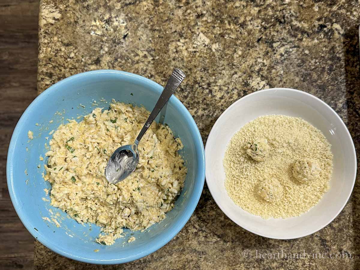 Crab ball mixture in a bowl next to a bowl of bread crumbs and three balls rolled into the breadcrumbs.
