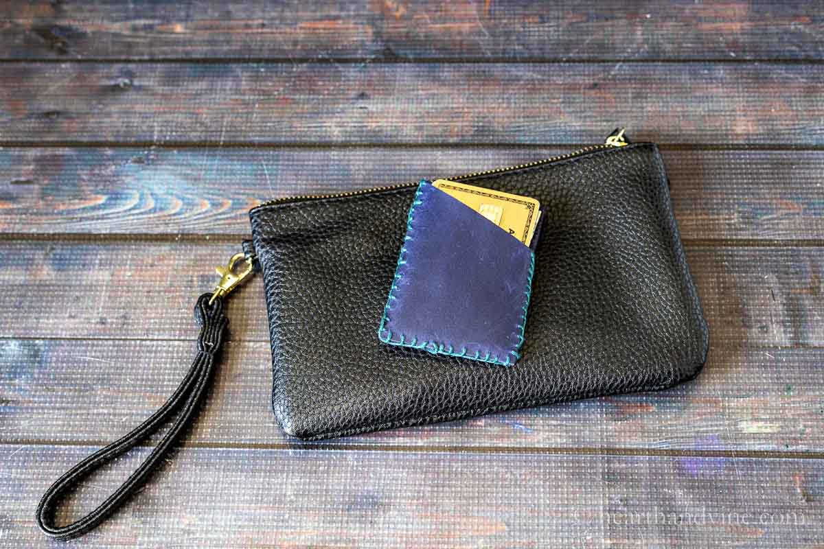 A small blue faux leather card holder on top of a small black clutch.