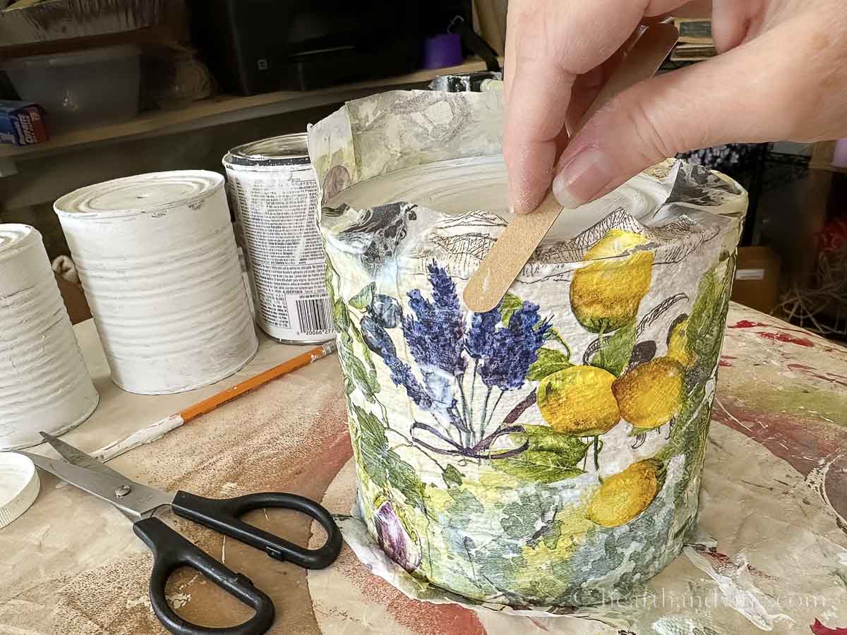 A nail file is used to file off the extra napkin from the top edge of the tin can.