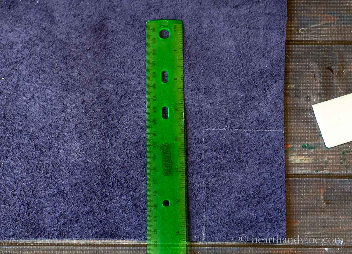 Blue faux leather, a green plastic ruler and a chalk marker outlining a rectangle on the edge.