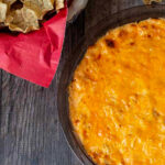 Partial view of a baked buffalo chicken dip next to a basket of tortilla chips.