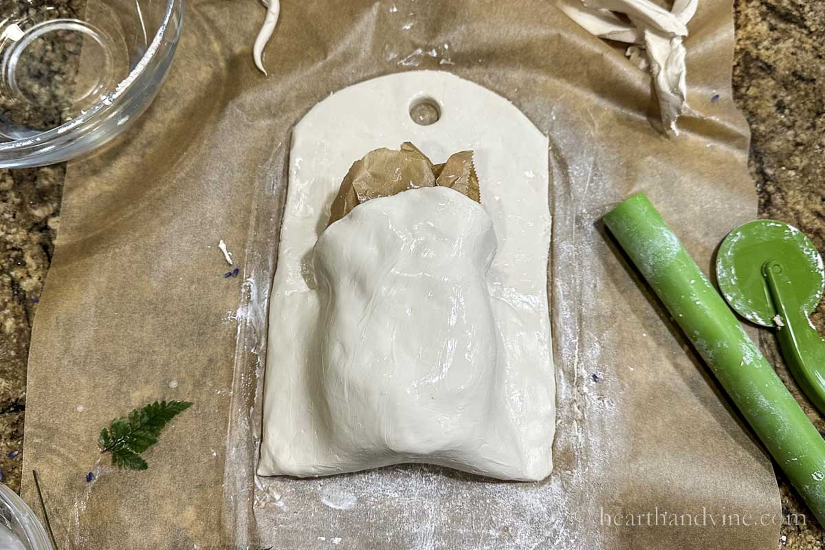 Clay wall pocket with parchment paper in the top and water all over to smooth out the clay.