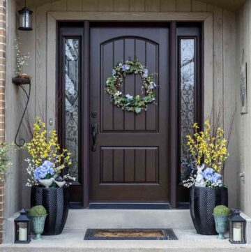Font porch decorated for spring with a morning glory wreath and pots of faux forsythia, blue flower and white berries.