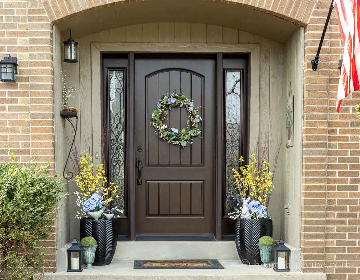 Here are some DIY spring front door porch decor ideas with faux flowers, cement birds and bunny, urns with moss balls and a spring wreath. 