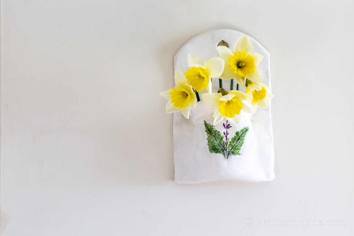 Clay wall pocket with fresh daffodils inside.