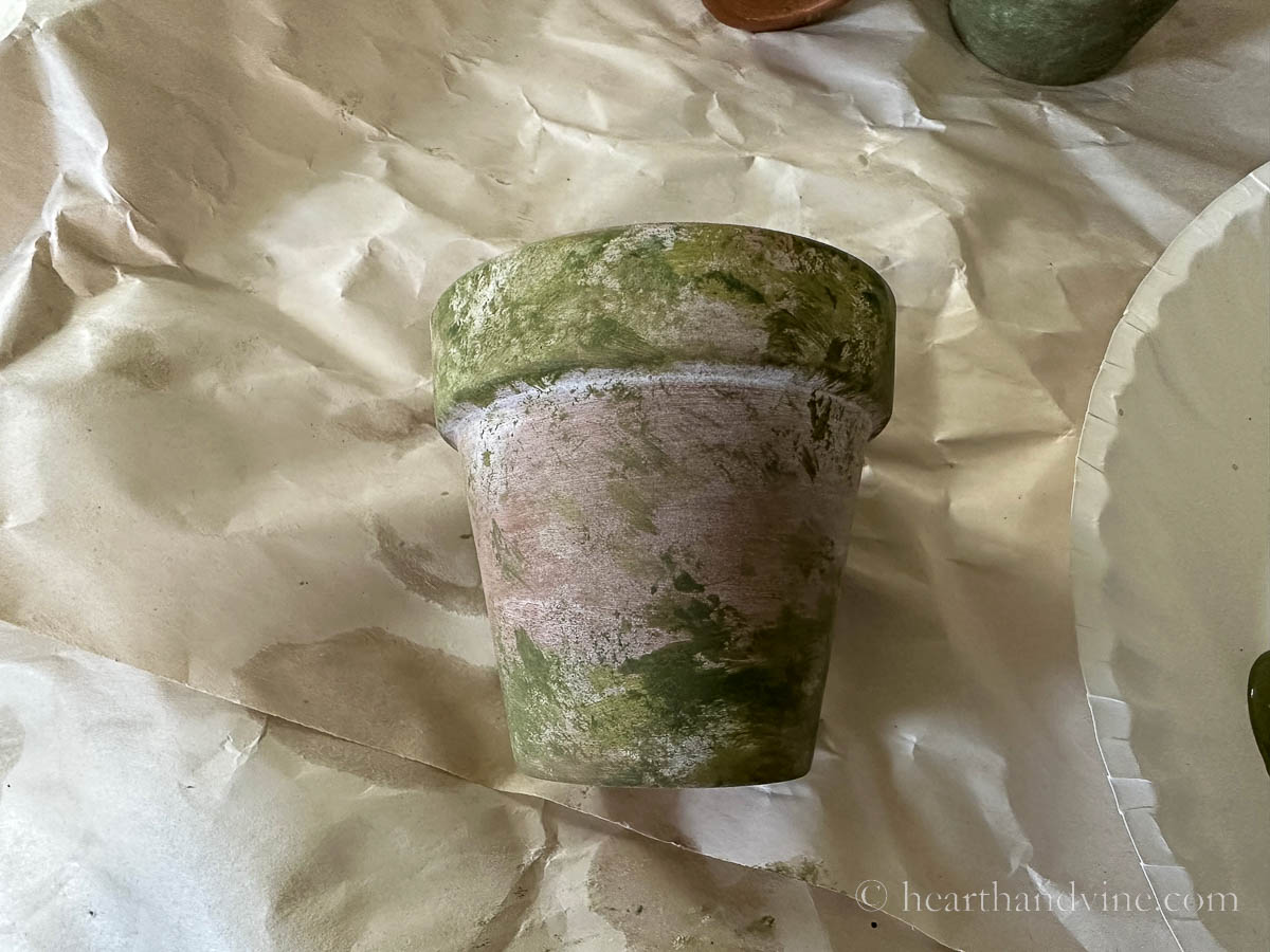 Small clay pot aged with paint in shades of moss green and some white.