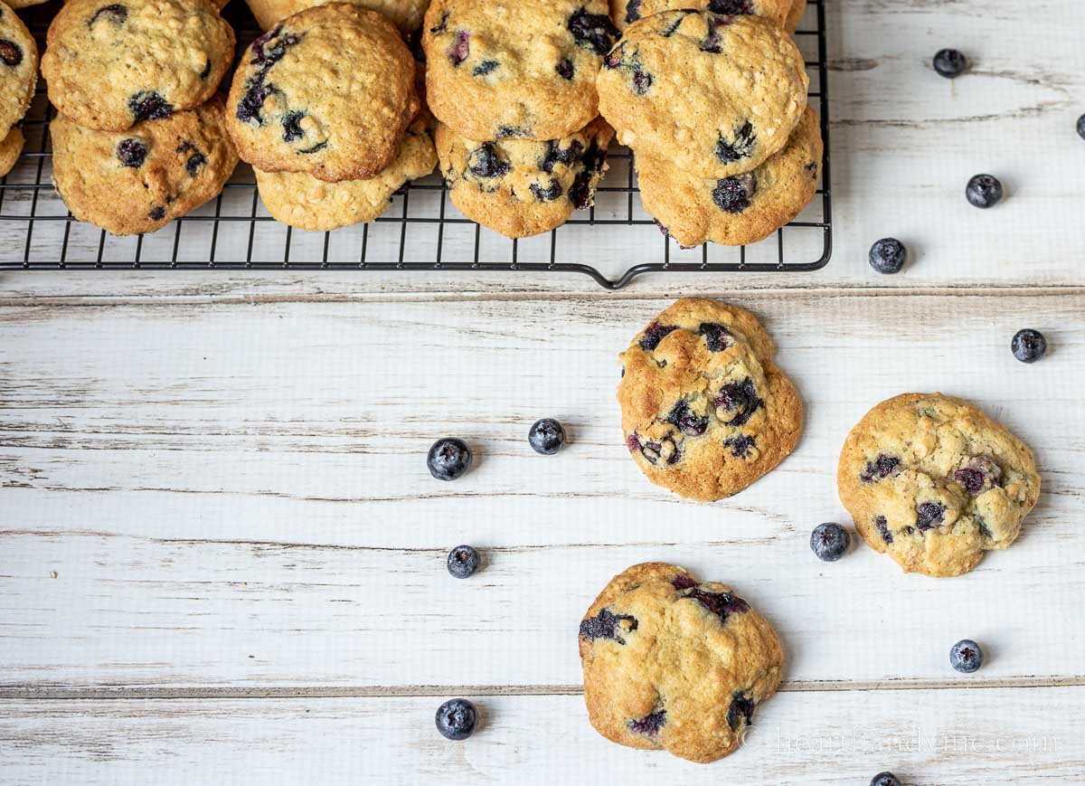 Golden brown blueberry cookies on a cooling rack and three on the table with fresh blueberries scattered around.