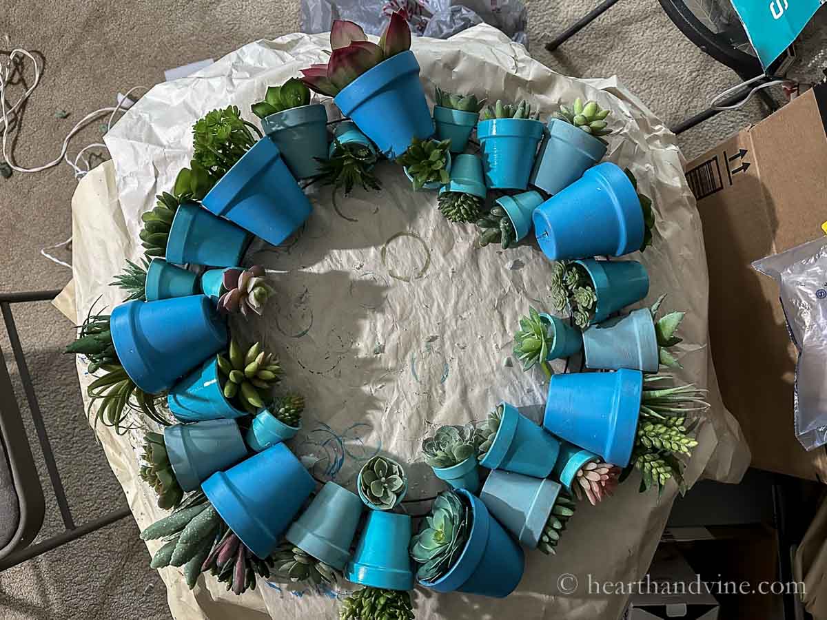 The finished terracotta pot wreath with faux succulents inside on a craft table.