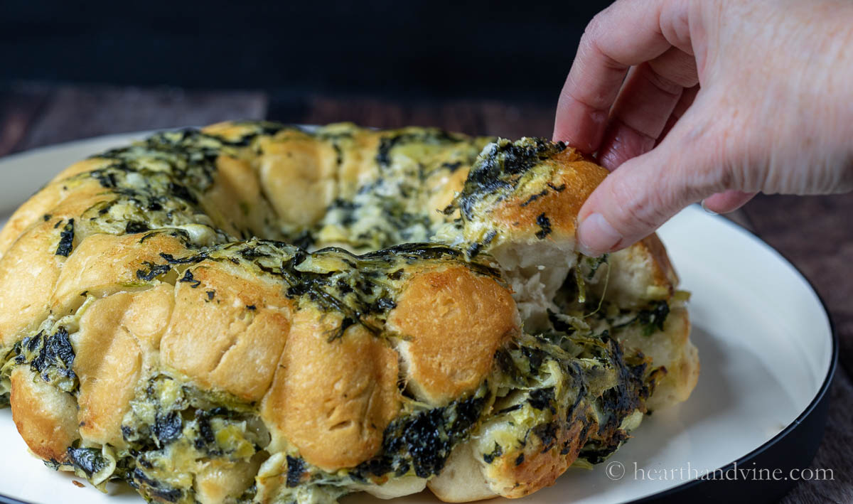 A hand pulling off a piece of the spinach artichoke bread.