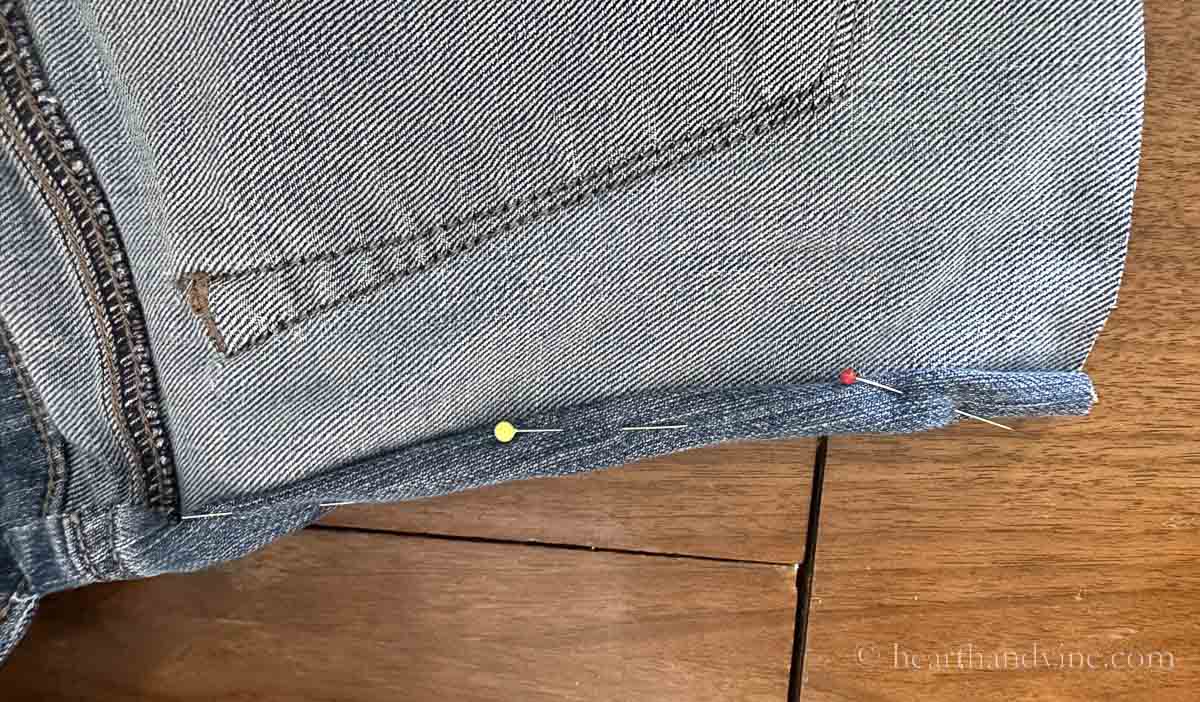 The raw edge of the jeans rolled over and pinned in place.