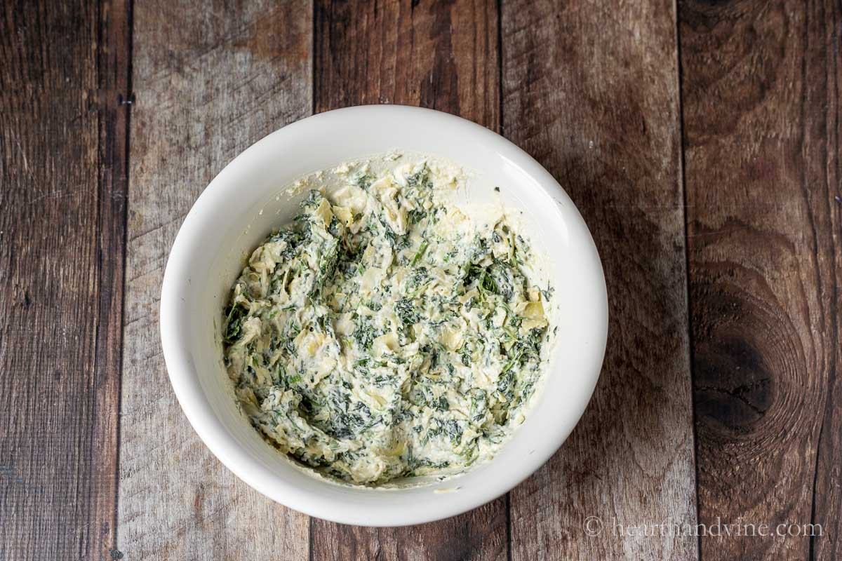 Spinach, artichokes, parmesan cheese and mayo mixed together in a bowl.