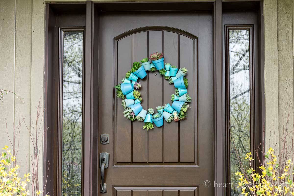 A blue themed terracotta pot wreath with artificial succulents plants on a front door.