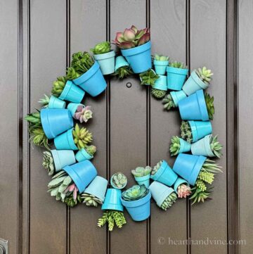 Terracotta pot wreath painted in shades of blue with faux succulents hanging on a door.
