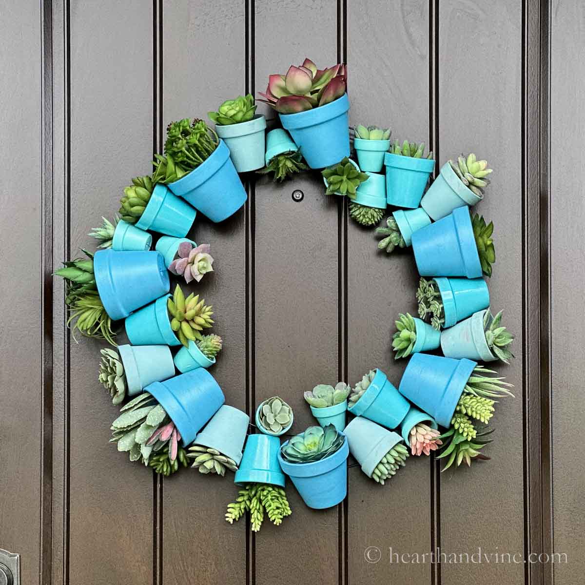 Terracotta pot wreath painted in shades of blue with faux succulents hanging on a door.