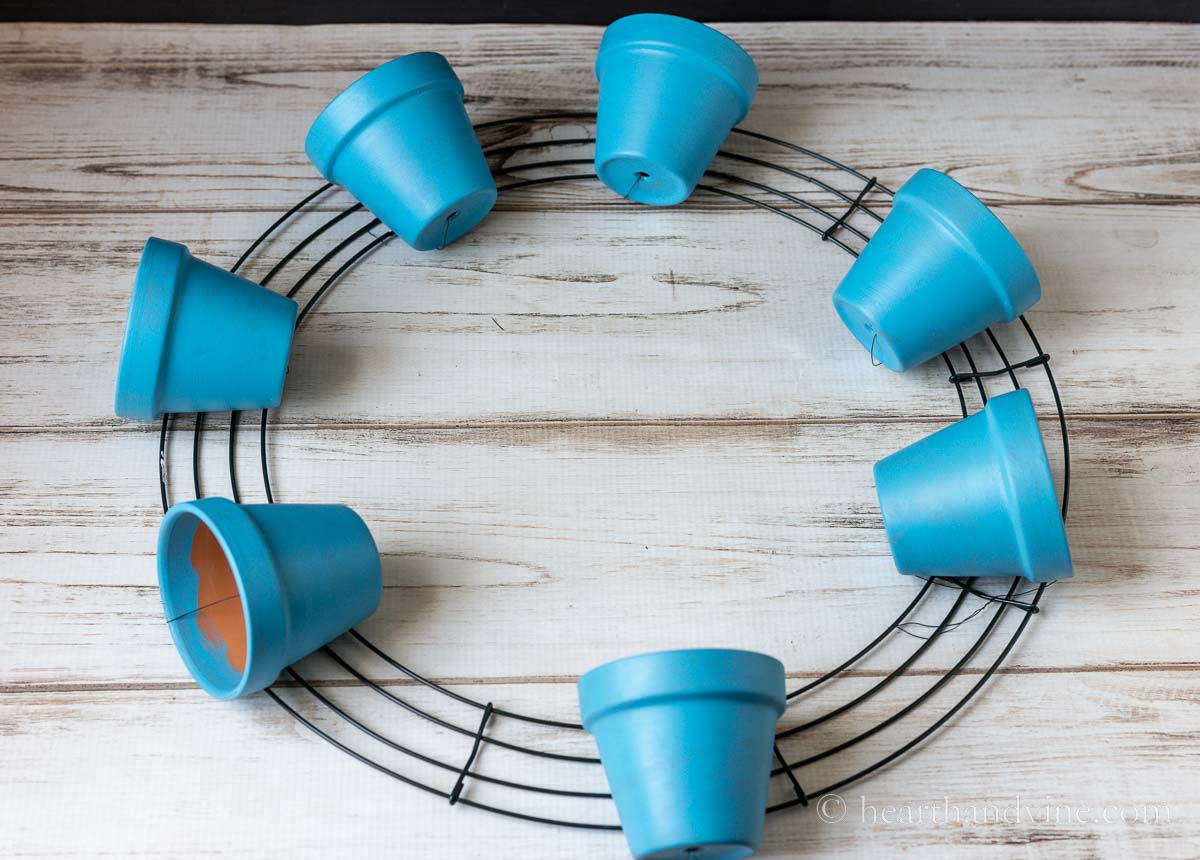 Seven 3 inch blue clay pots tied on a wire wreath frame in equal increments.