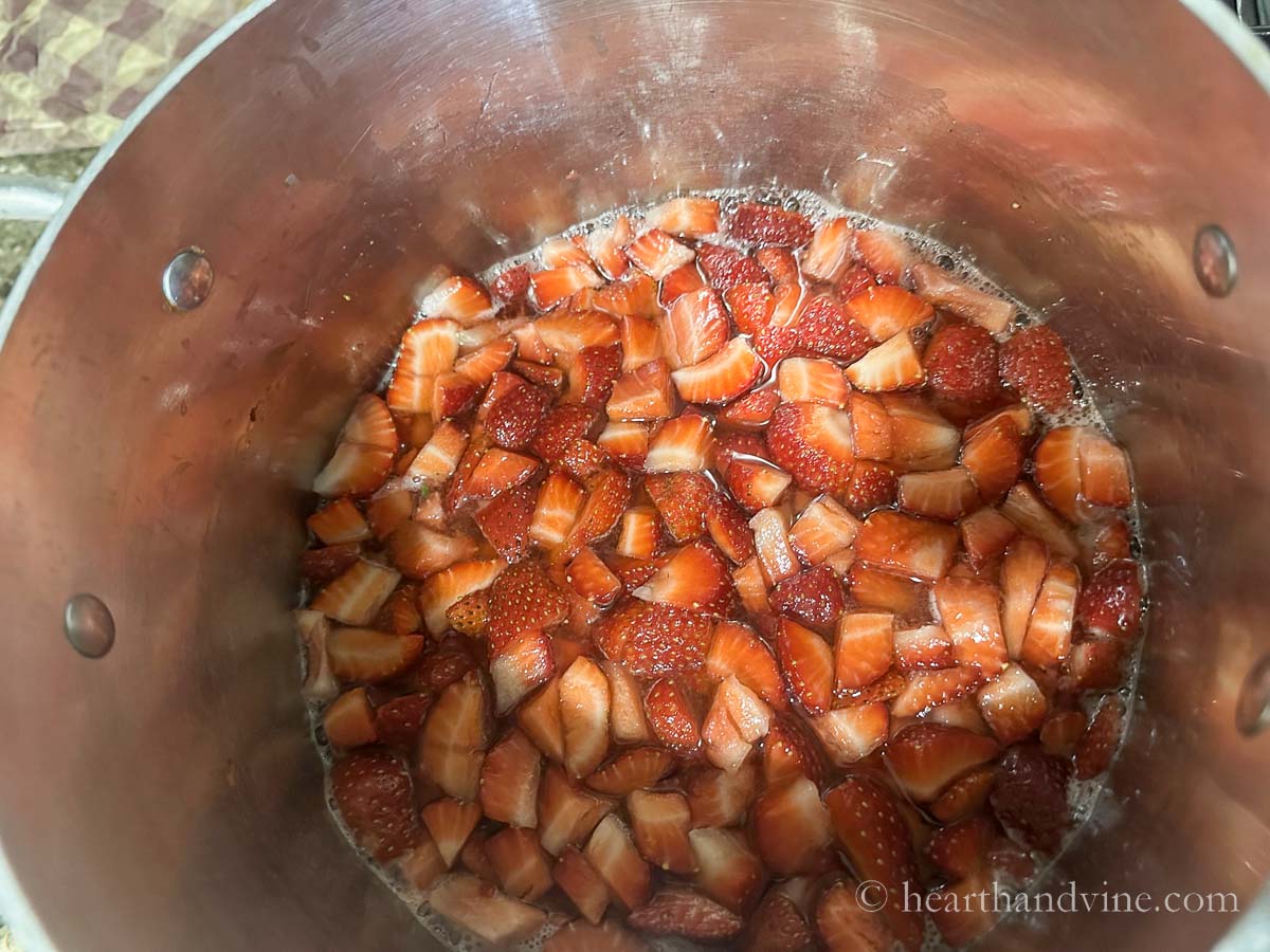 Chopped strawberries, water, sugar and lemon juice simmering in a pot.