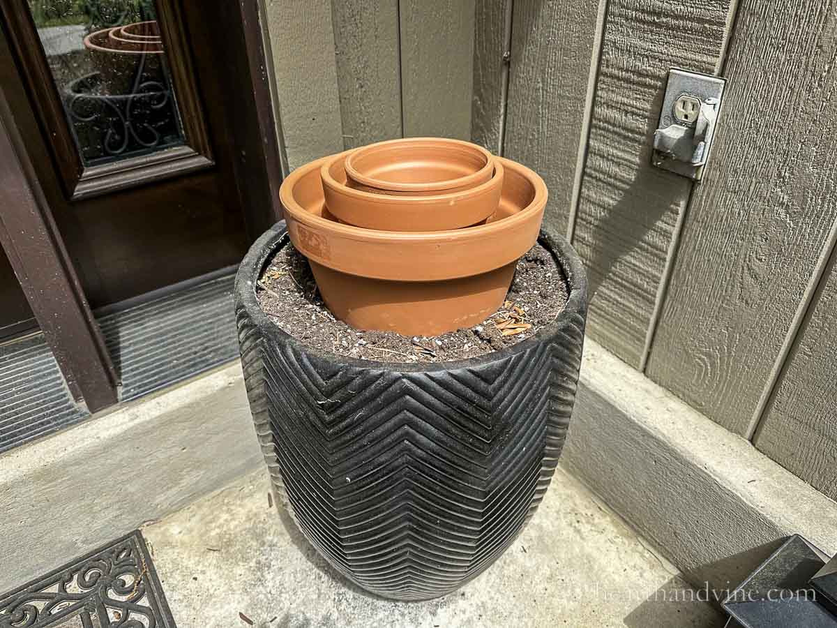 Three clay pots nested on top of a large black planter.
