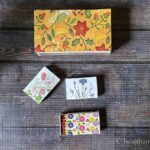 One large matchboxes covered in a country print and three small matchboxes with floral prints.