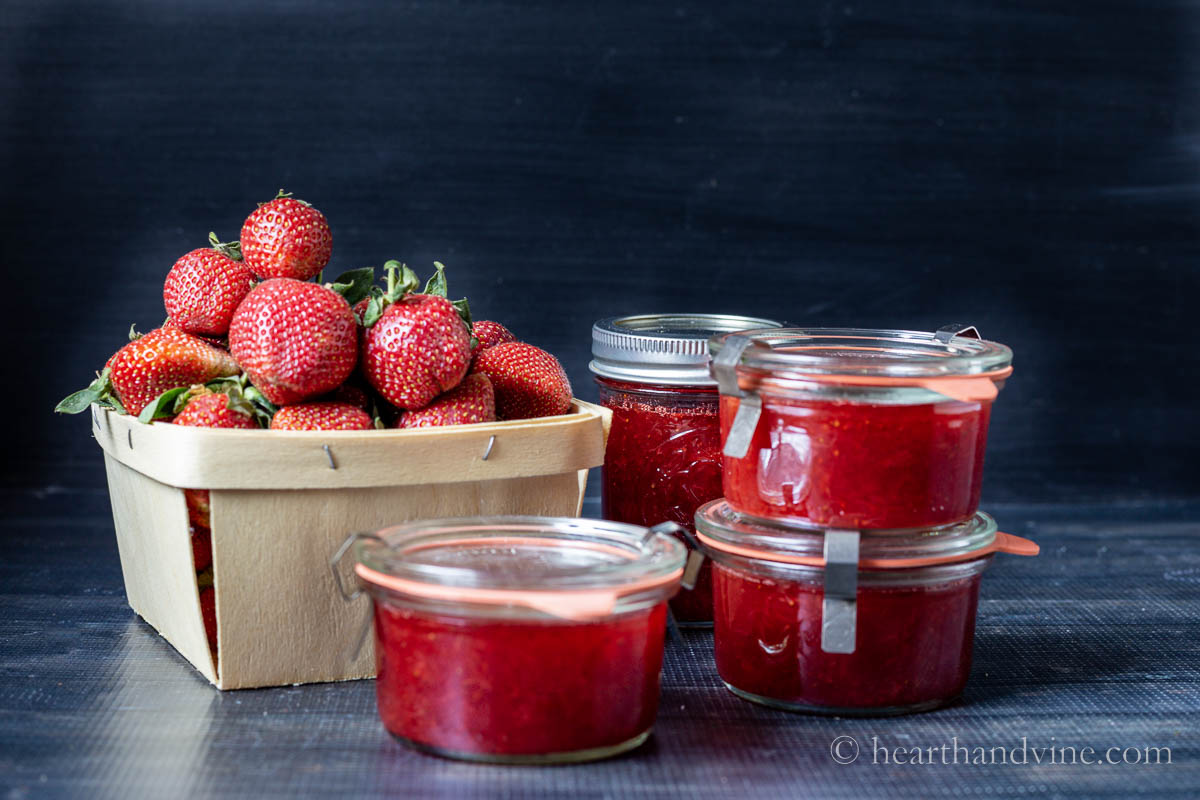 Basket of fresh strawberries next to a few jars of strawberry jam.