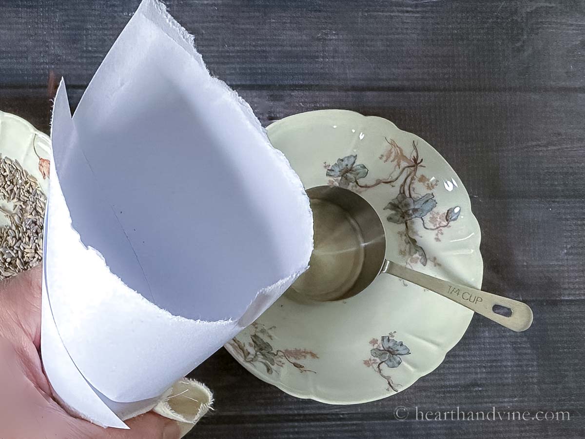 A hand holding a paper funnel near a measuring cup and bowl.