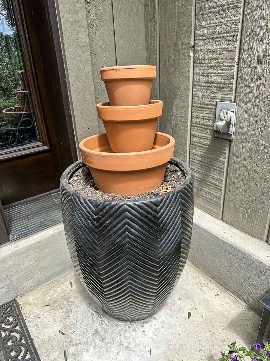 View from the side of three terra cotta pots stacked on top of a large black planter.