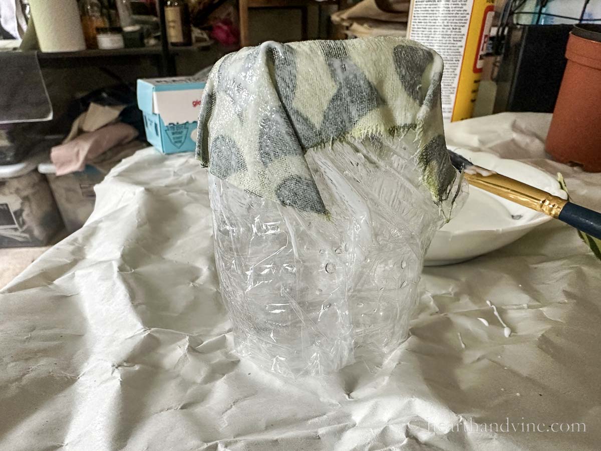 Plastic covered water bottle bottom upsidedown with a piece of fabric covering the bottom with glue.