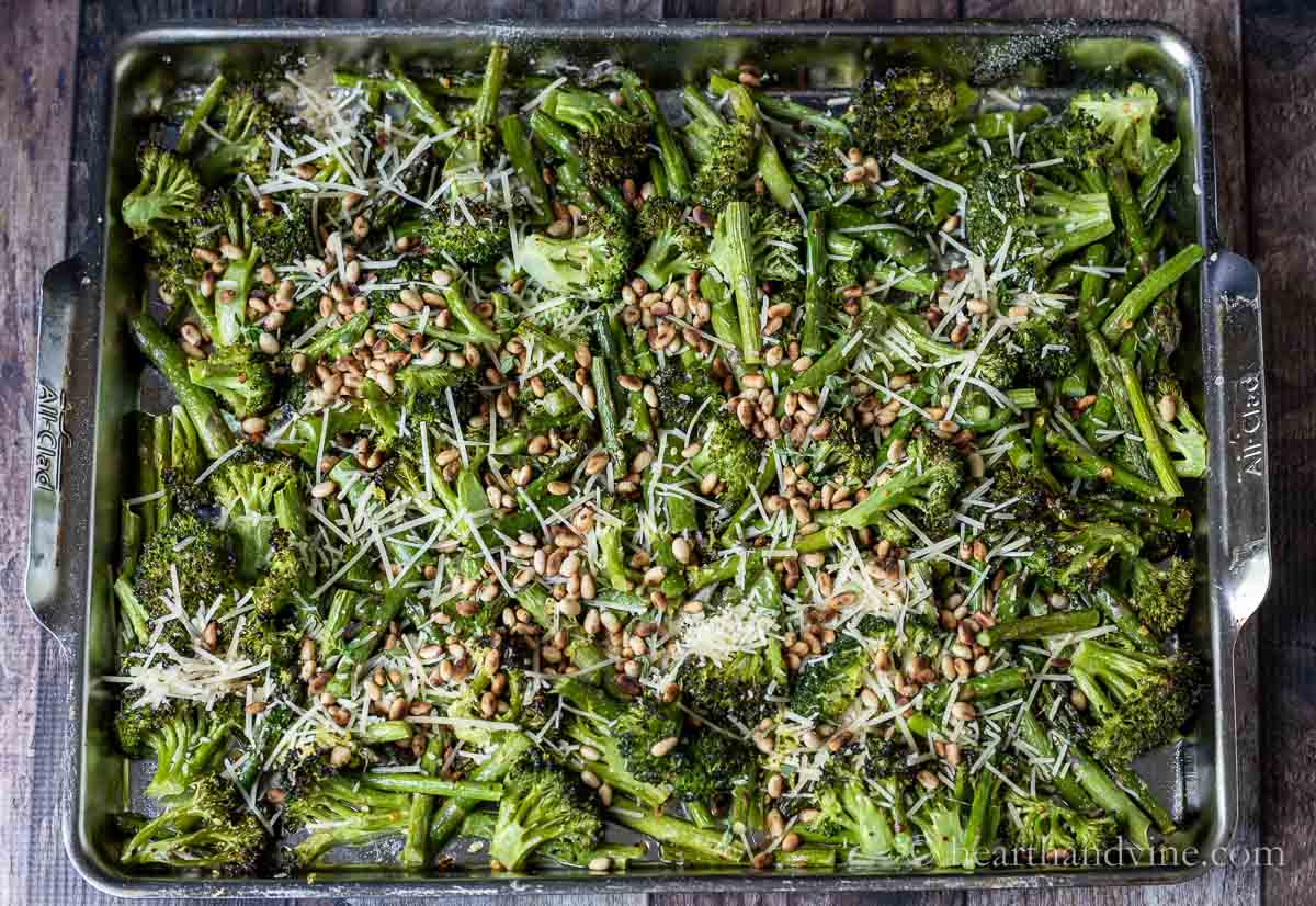 Roasted broccoli and asparagus on a baking sheet with toasted pine nuts and cheese sprinkled over the top.